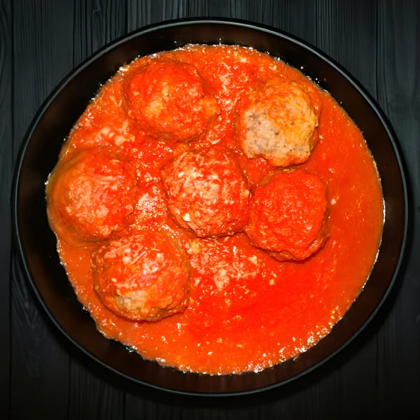Tony's Pizza meatballs in rich red marinara sauce, served in a black bowl on a dark wooden table.